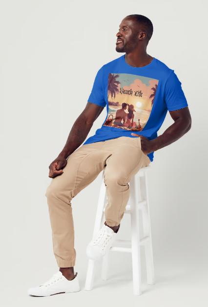 This is a model wearing a t-shirt entitled "Beach Life" men's graphic t-shirt. The shirt itself is blue in color. Made of soft and breathable cotton, this shirt embodies the perfect beach day with a romantic scene full of warm colors, it features a couple enjoying a sunset picnic surrounded by palm trees by the ocean. Let the bold design and adventurous spirit inspire your next adventure!" This is a Mike Roxly collection T-shirt